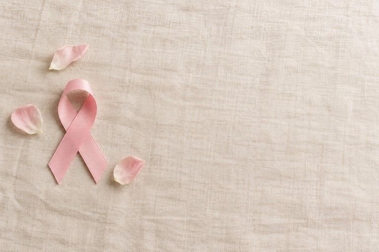 A pink awareness ribbon and petals on cream linen